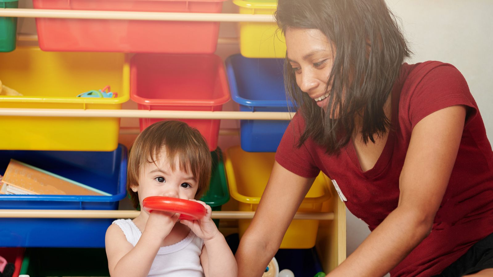Female child care professional playing with young child and colorful toys.
